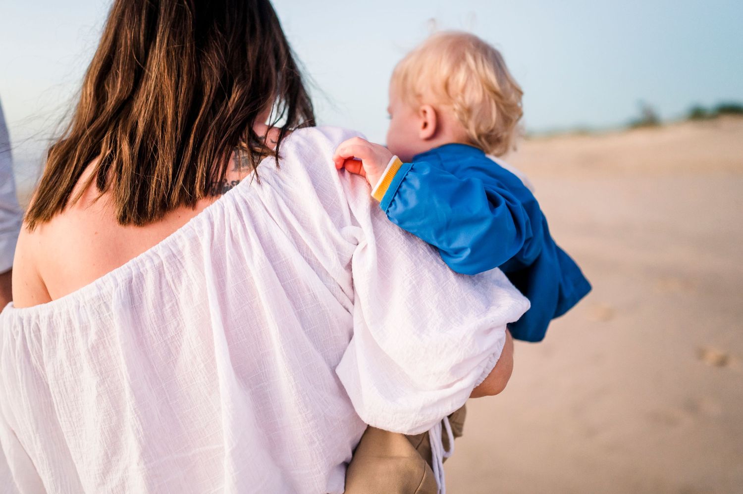 Woman in white holding small child on sunny beach.