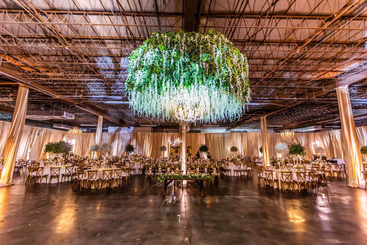Wide angle view of an elegant ballroom with hanging greenery and crystal lighting fixtures.