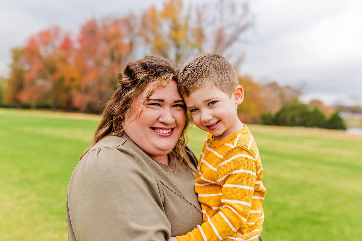 Two people sharing a joyful embrace outdoors on a beautiful fall day with colorful trees in the background.