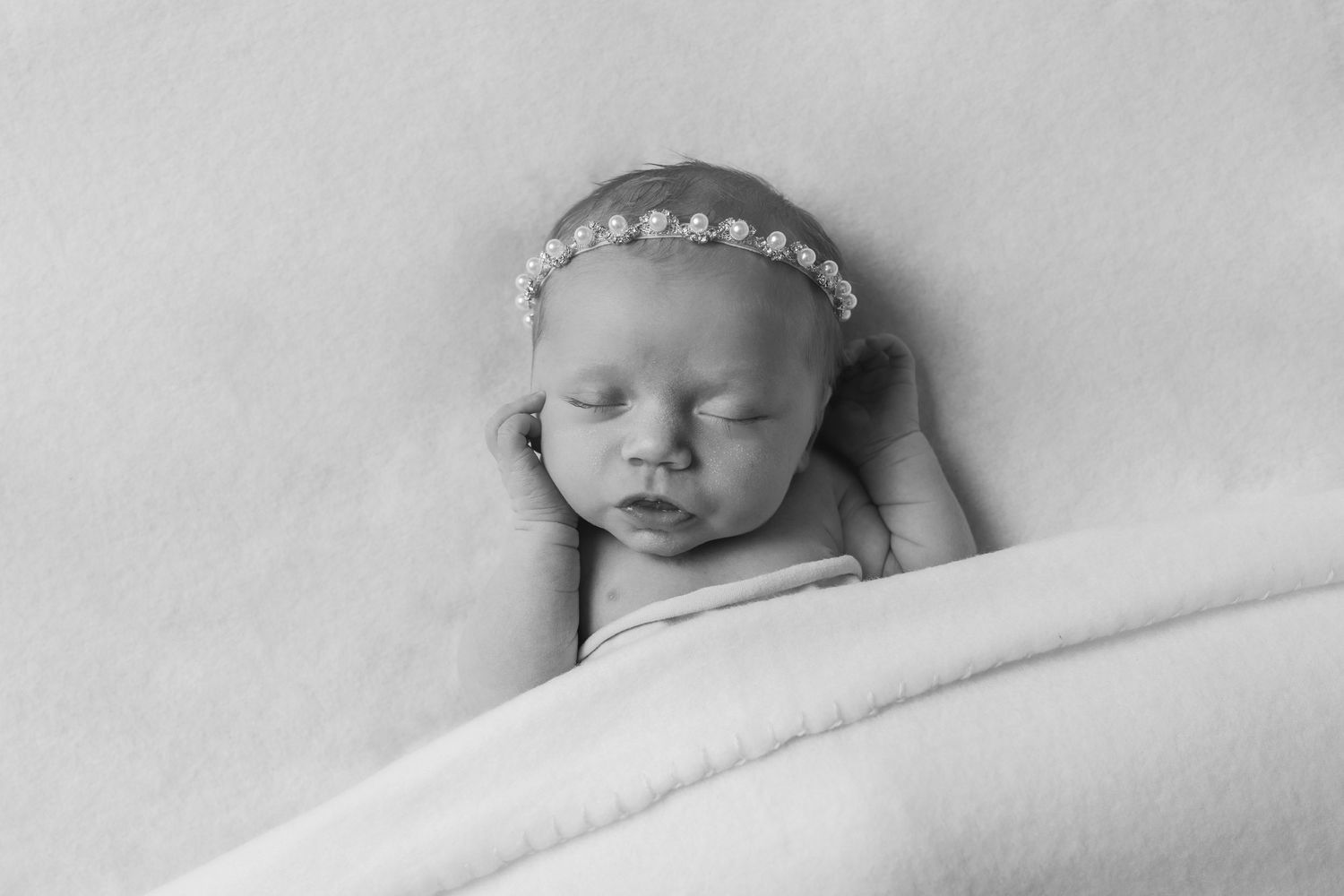 Black and white portrait of a sleeping newborn wearing a delicate floral headband.