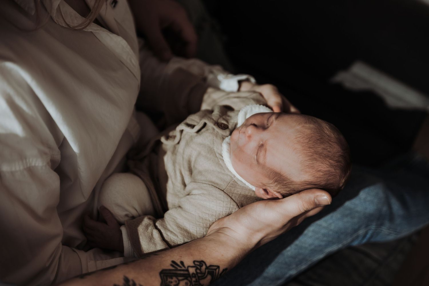 Intimate low-light portrait of sleeping infant being cradled in white clothing.