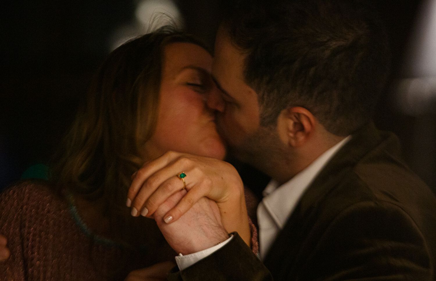 Ari and Helena kiss, their faces slightly blurred as the focus is drawn to her new green engagement ring