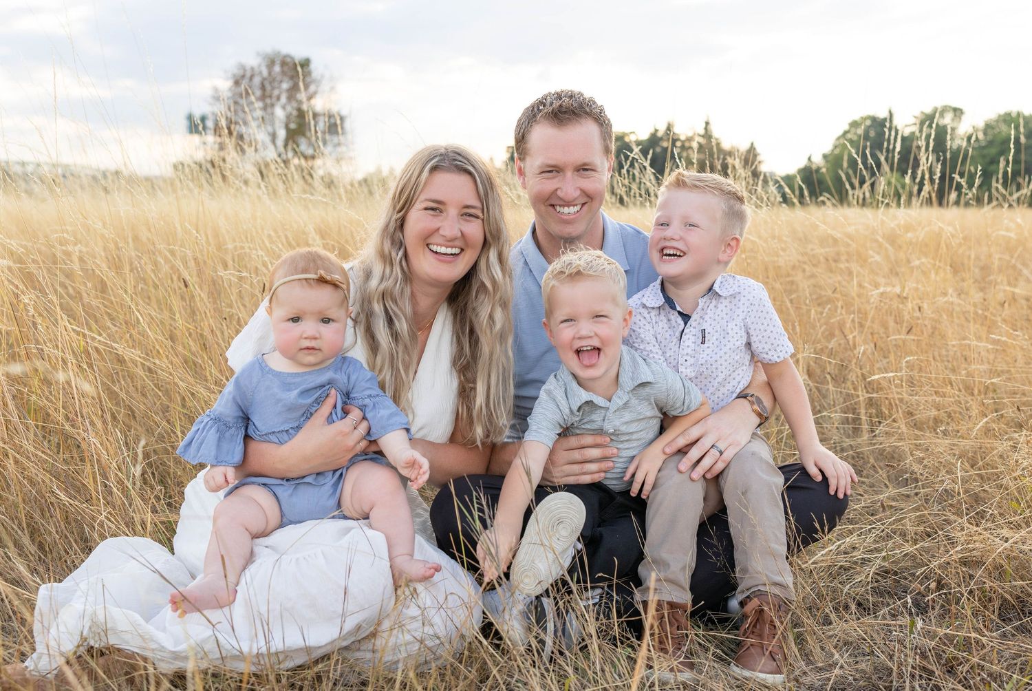 Happy family of five laughing together in a golden wheat field during a sunny outdoor photo session.