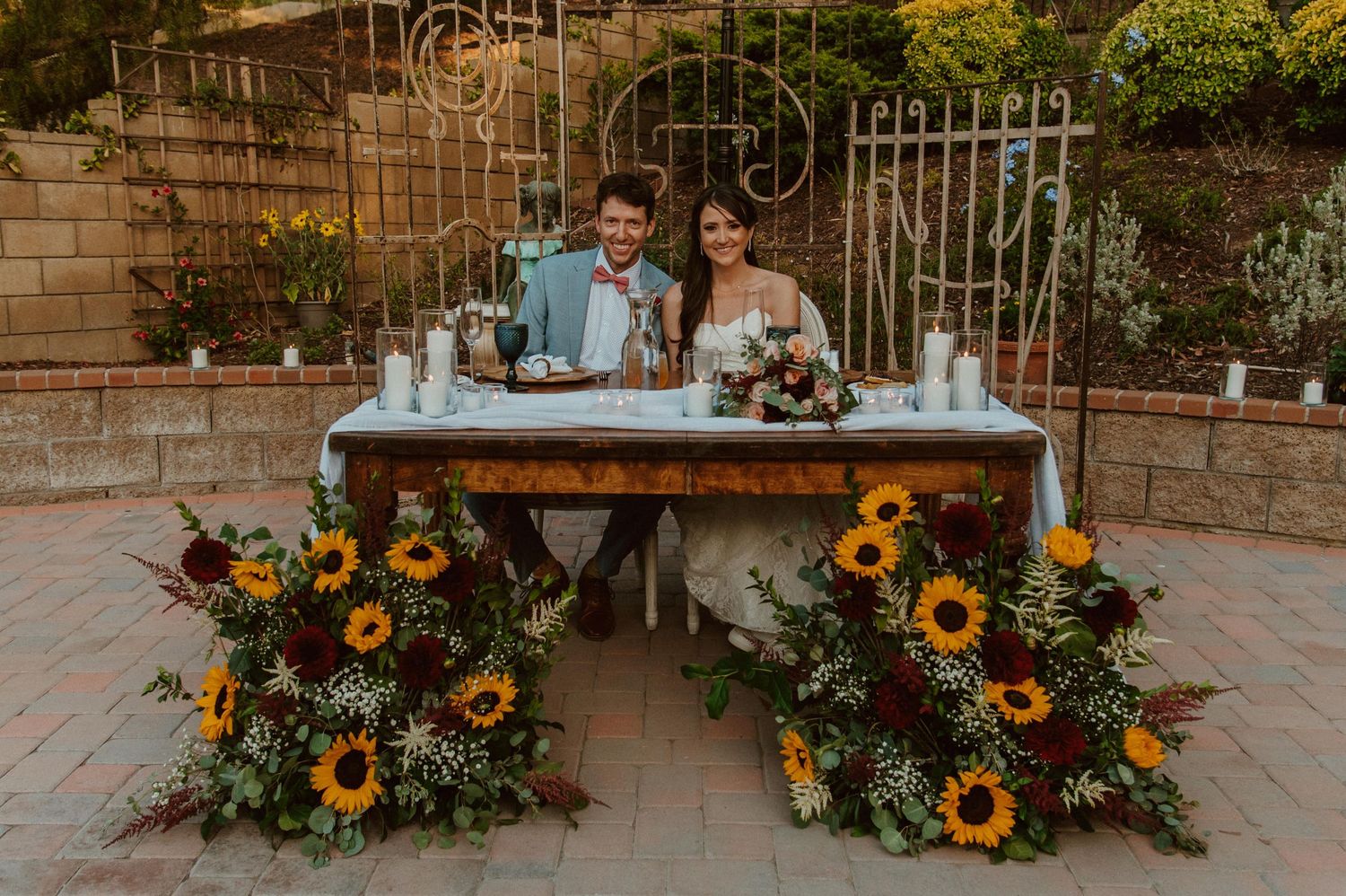 Outdoor wedding decor features sunflower arrangements on rustic benches.