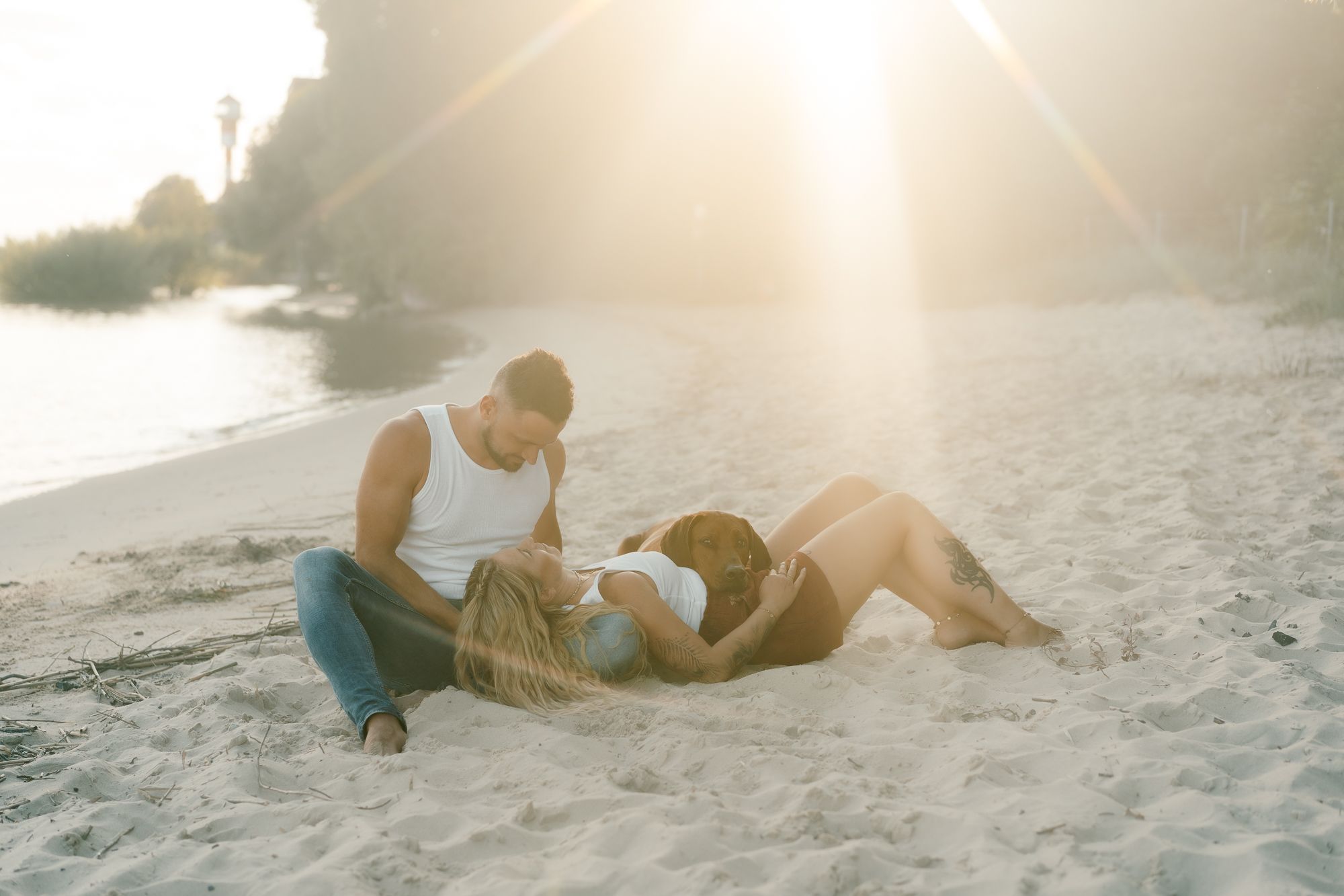 Couple and their chocolate lab dog enjoy a tender sunset moment on a sandy beach path.