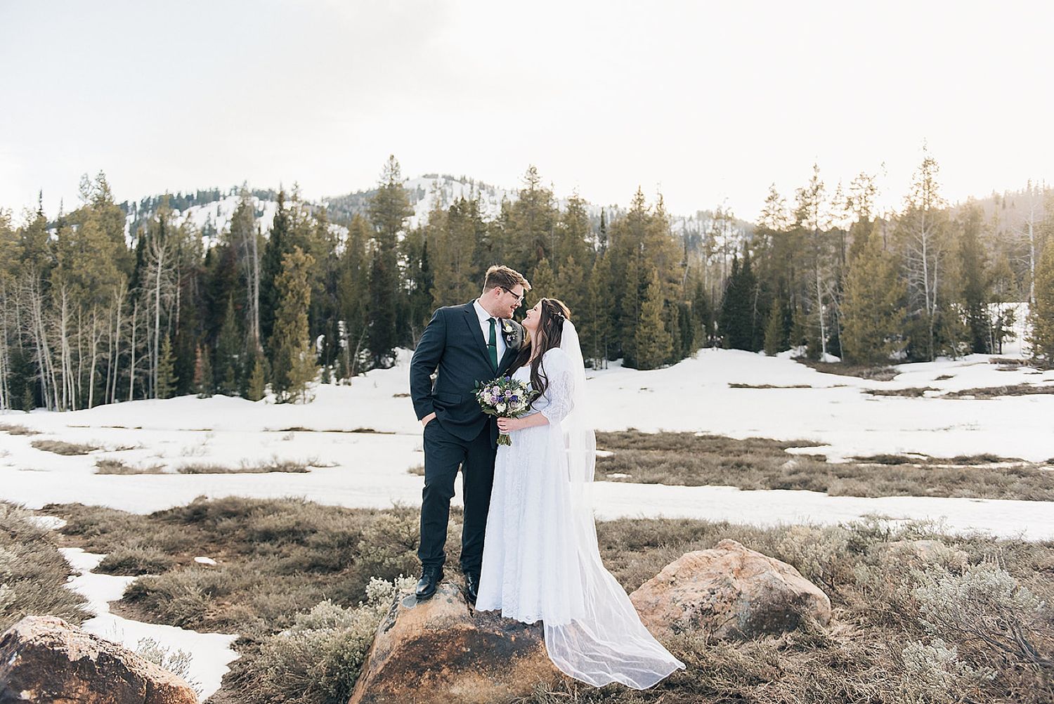 A wedding couple stands on a snowy mountain peak during their winter ceremony.
