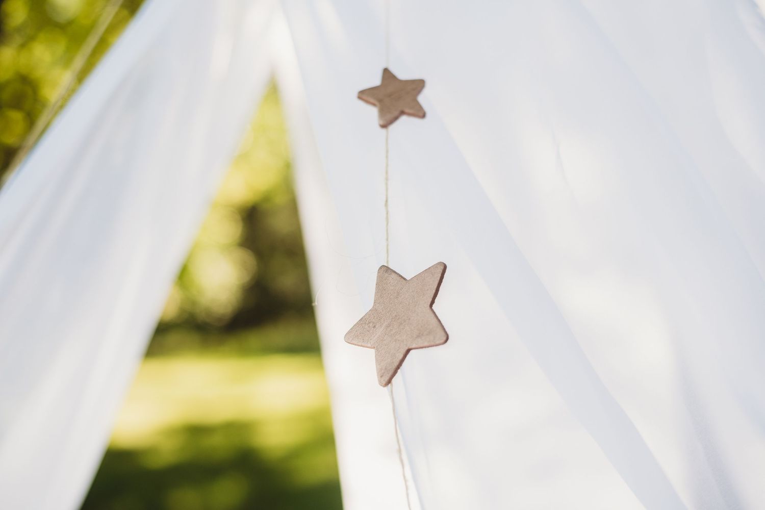 Decorative fabric stars hanging from white tent material in soft natural lighting.