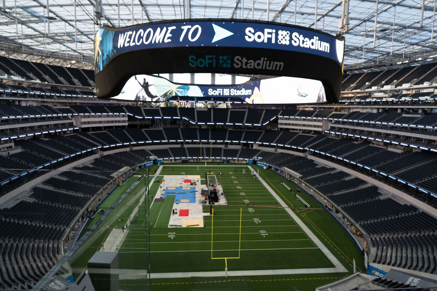 Interior view of empty SoFi Stadium with welcome message displayed on scoreboard.