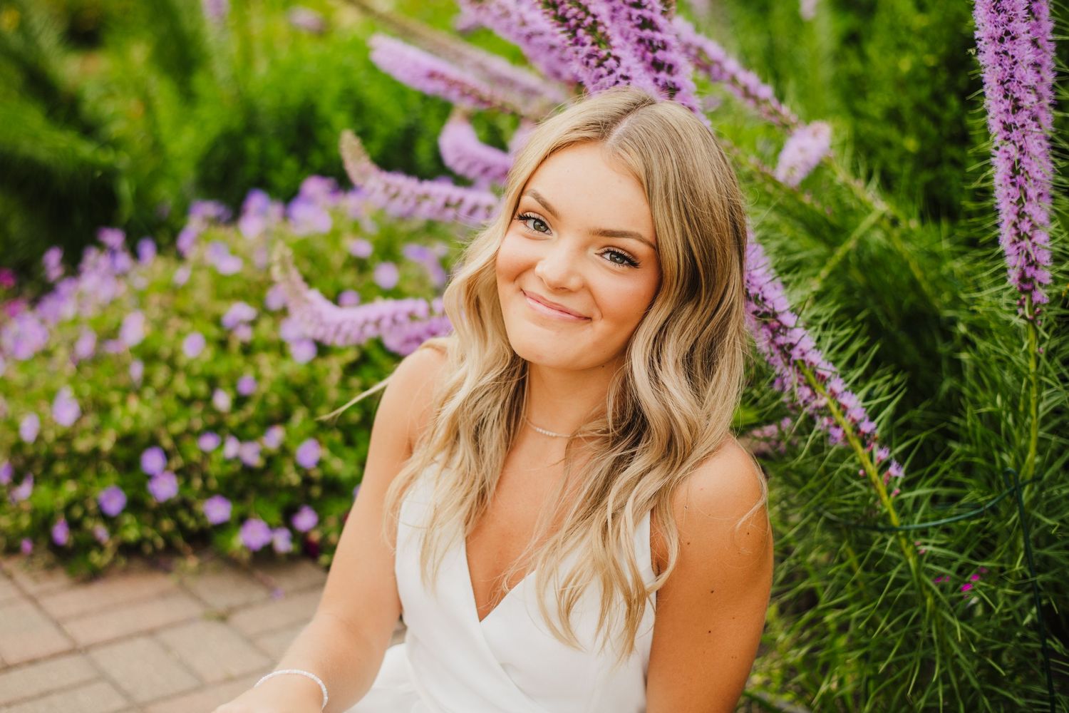 Portrait in a garden with purple flowers and greenery in the background.