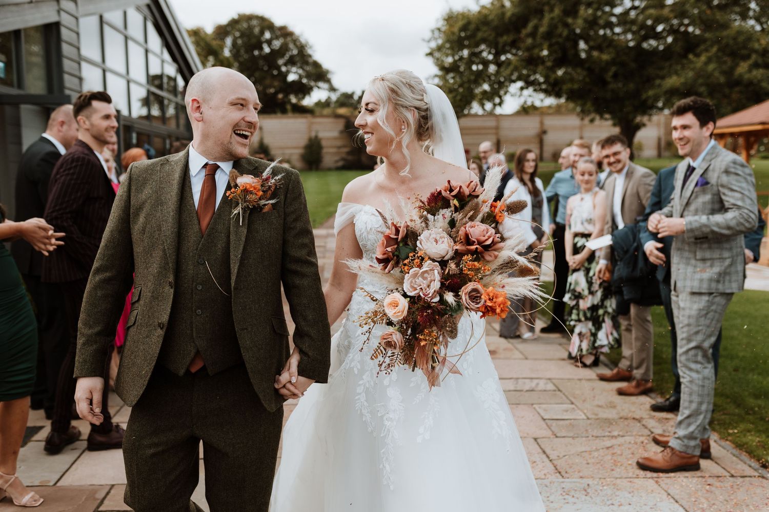 Wedding celebration on stone walkway with autumn-colored bouquet and gathering of guests.