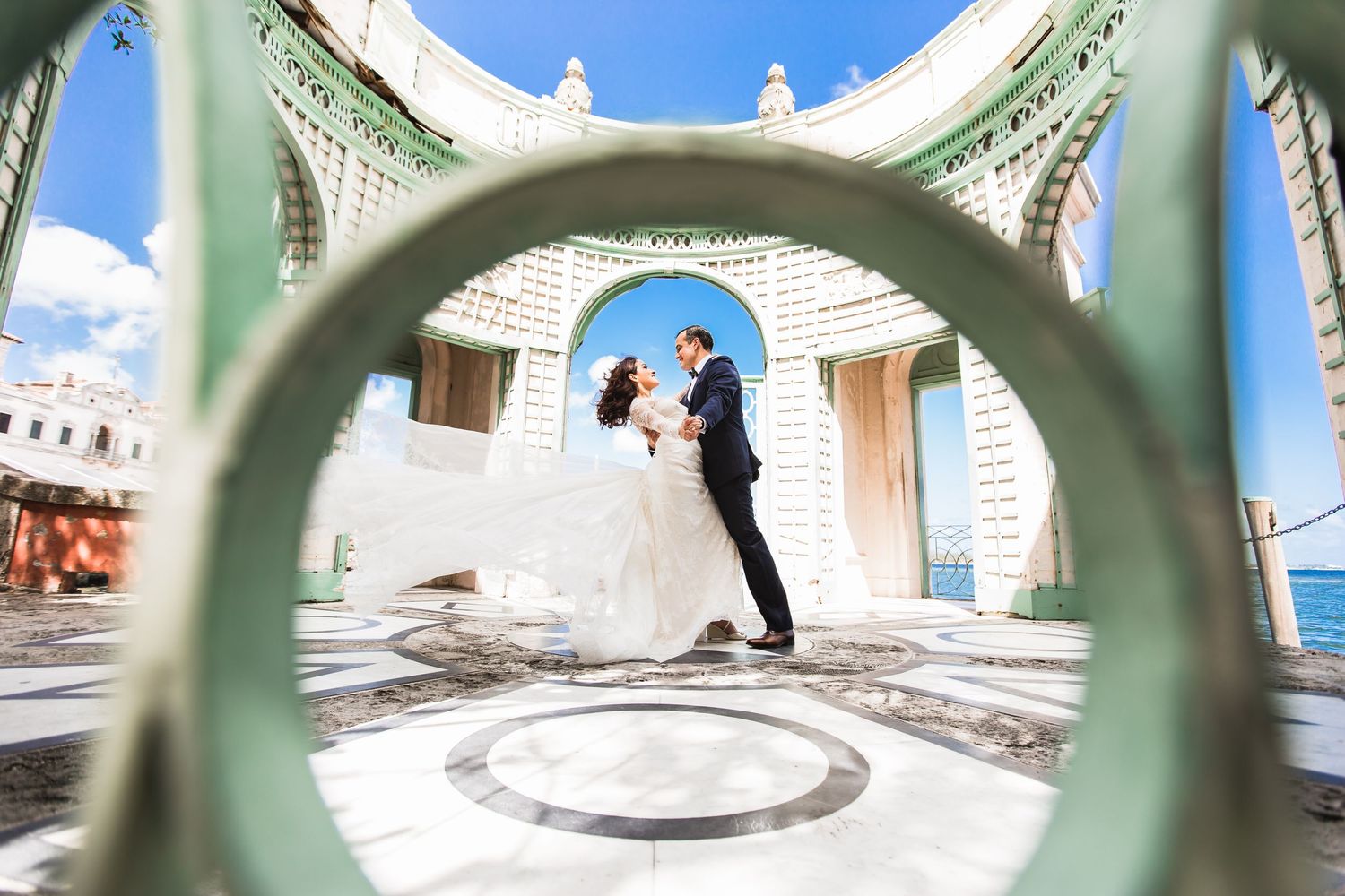 Artistic wedding photo through architectural arches with blue sky background.