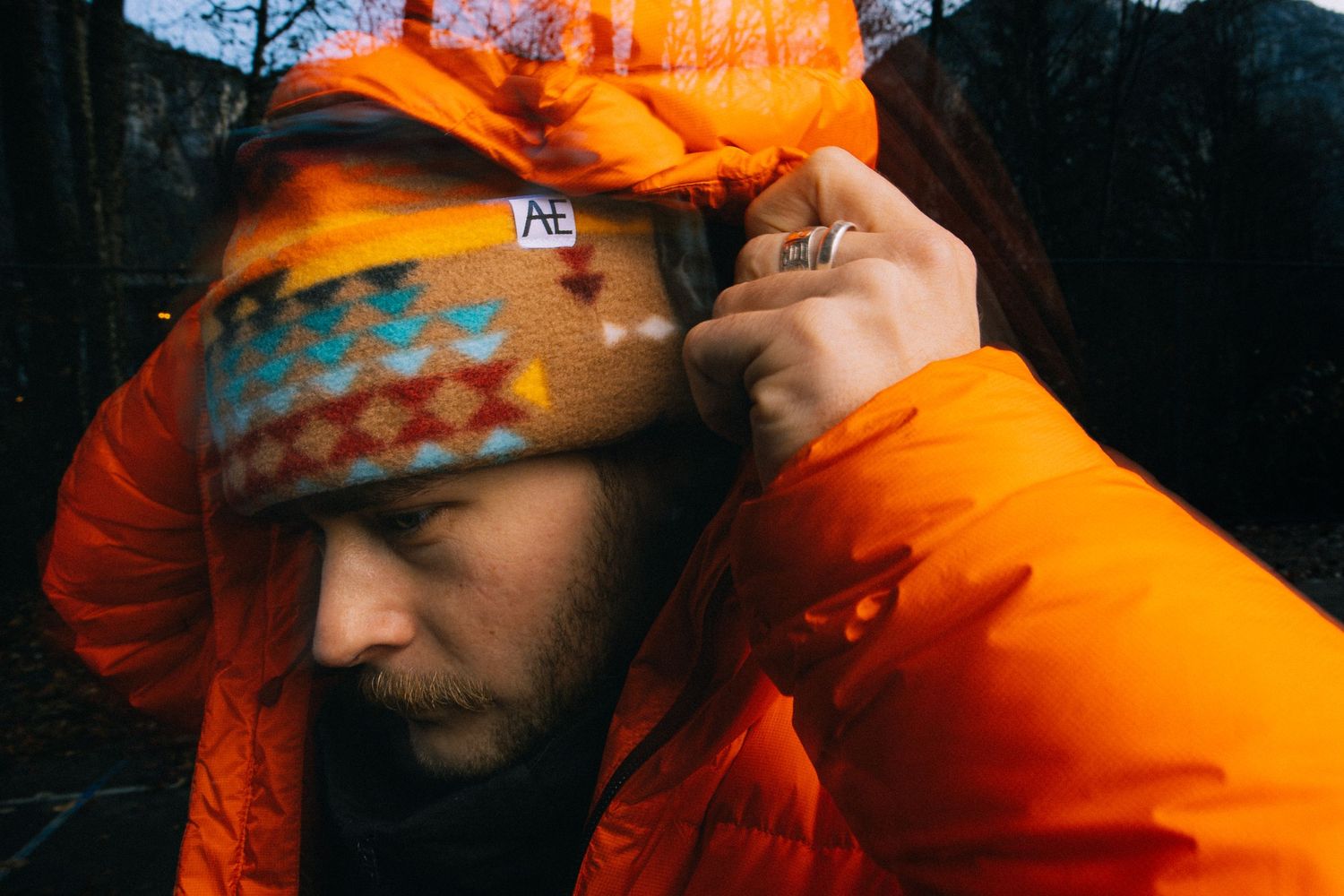 Person in bright orange winter jacket and patterned beanie shown in moody lighting.