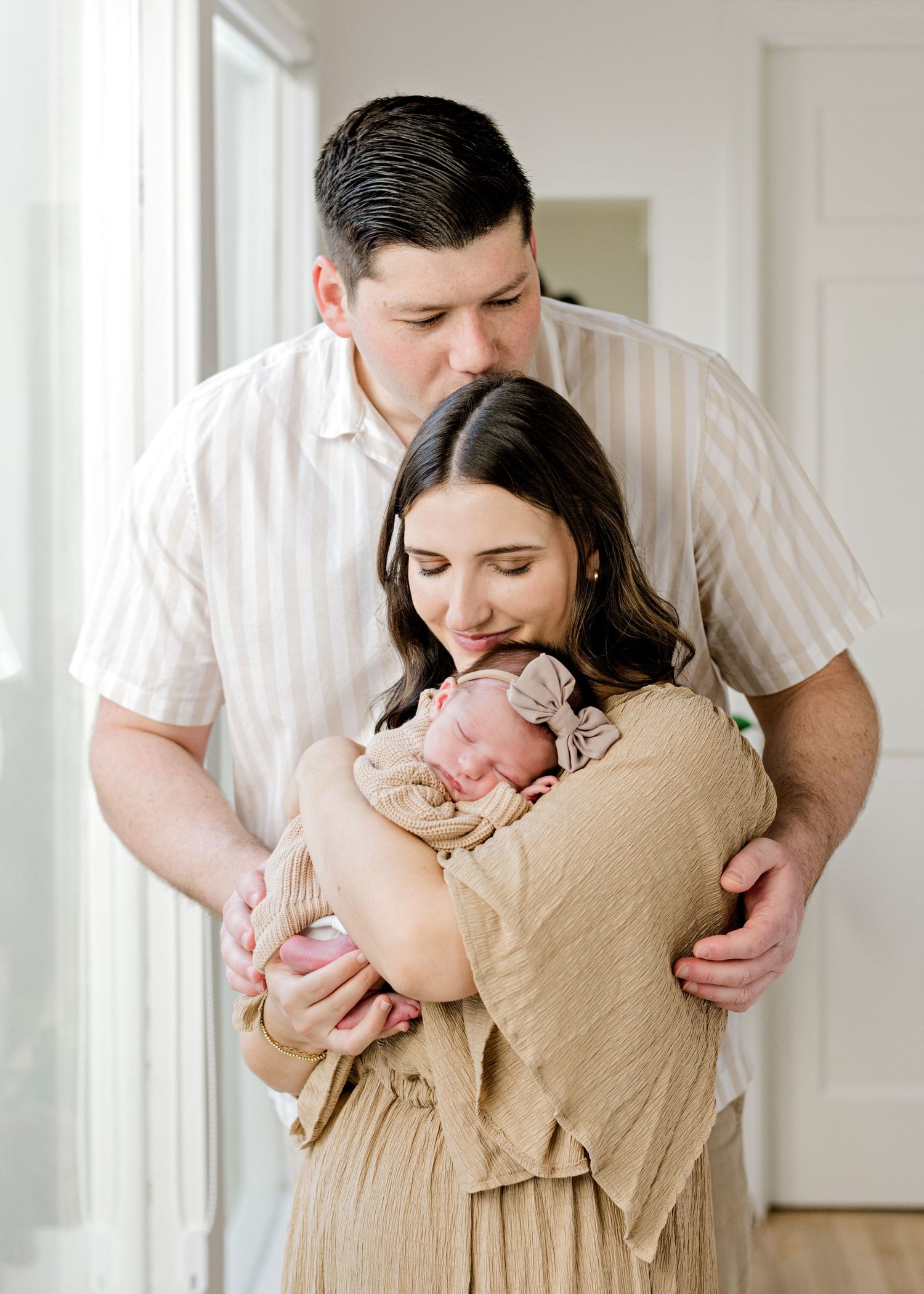 new mom holding her newborn baby on her shoulder as she smiles down at her and dad kisses mom's head
