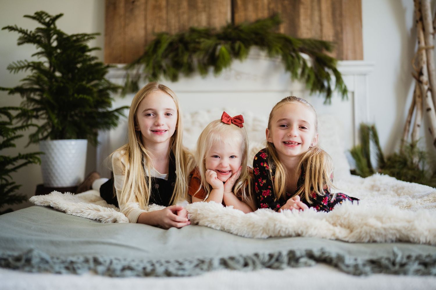 Three young children lying on white fur blanket with holiday decor in background.