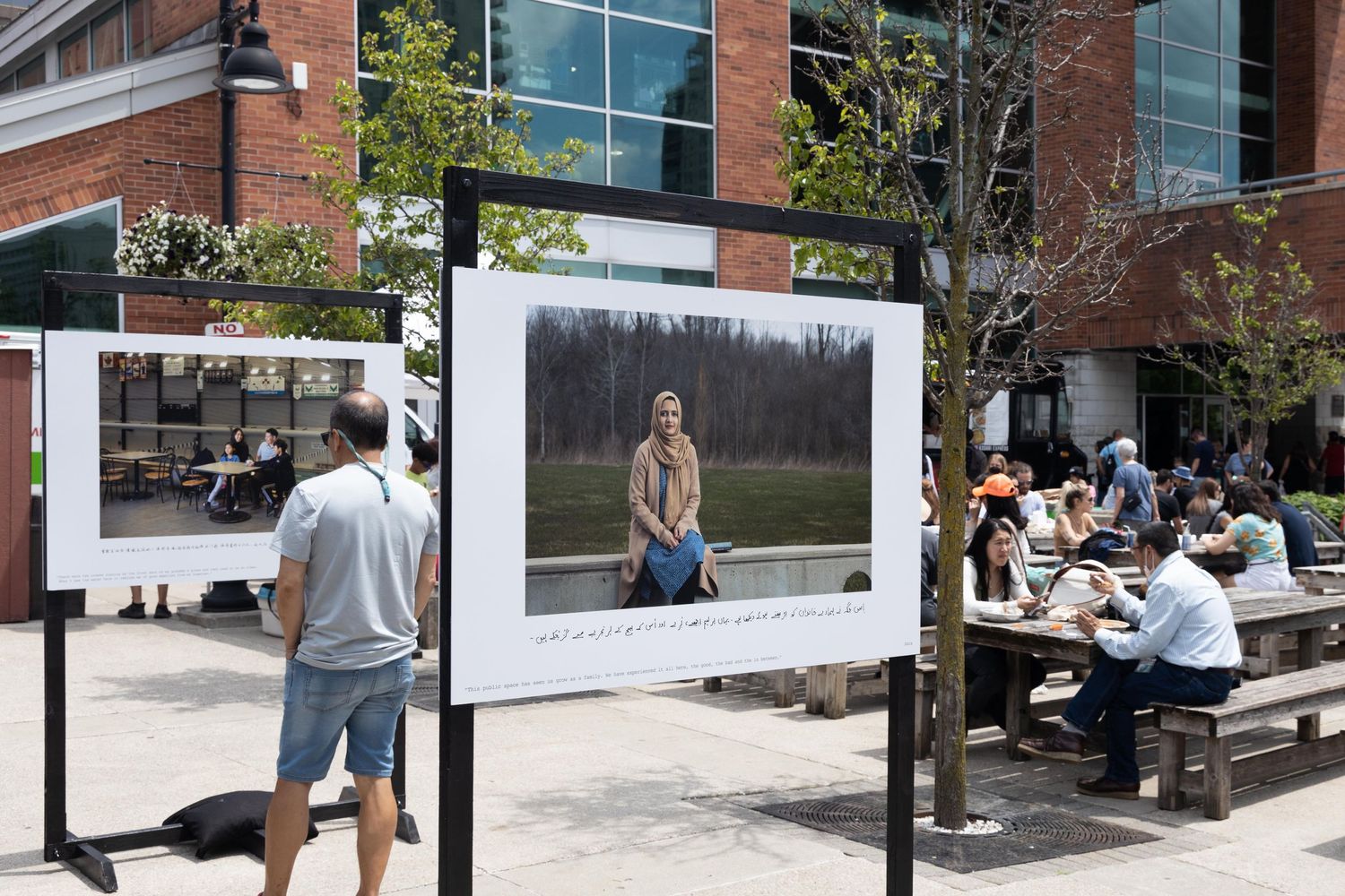 Large framed photograph displayed outdoors with people viewing art installation on campus.