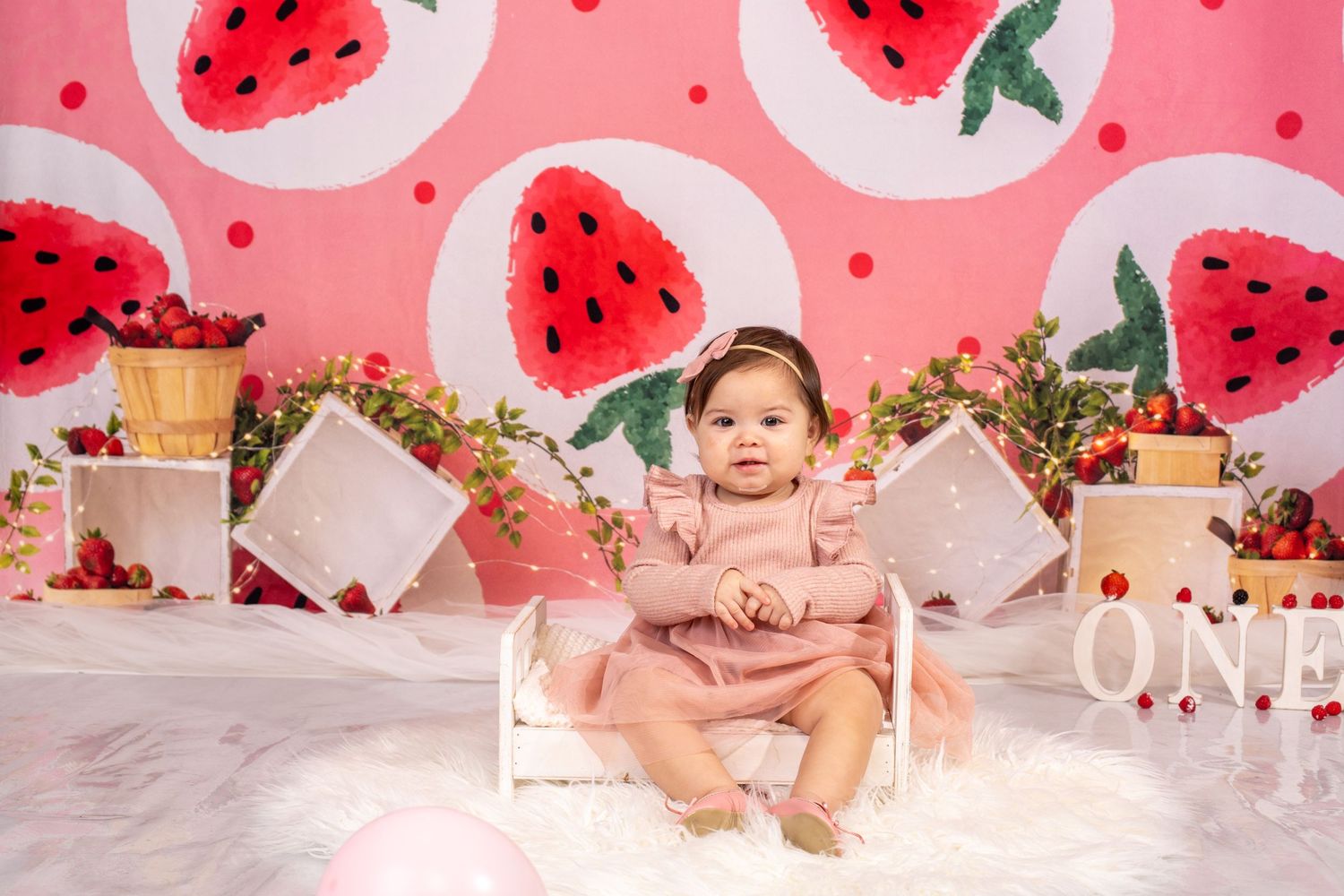 Baby photo session with watermelon-themed backdrop and pink decorative elements.