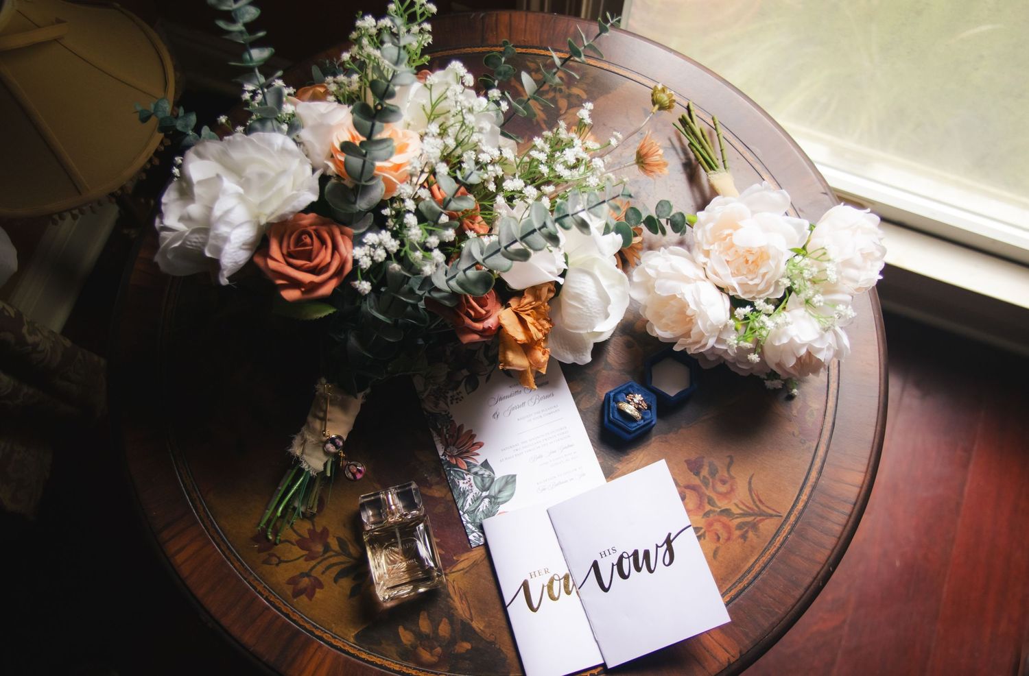 Wedding detail shot of floral arrangement with roses and a card on wooden table.