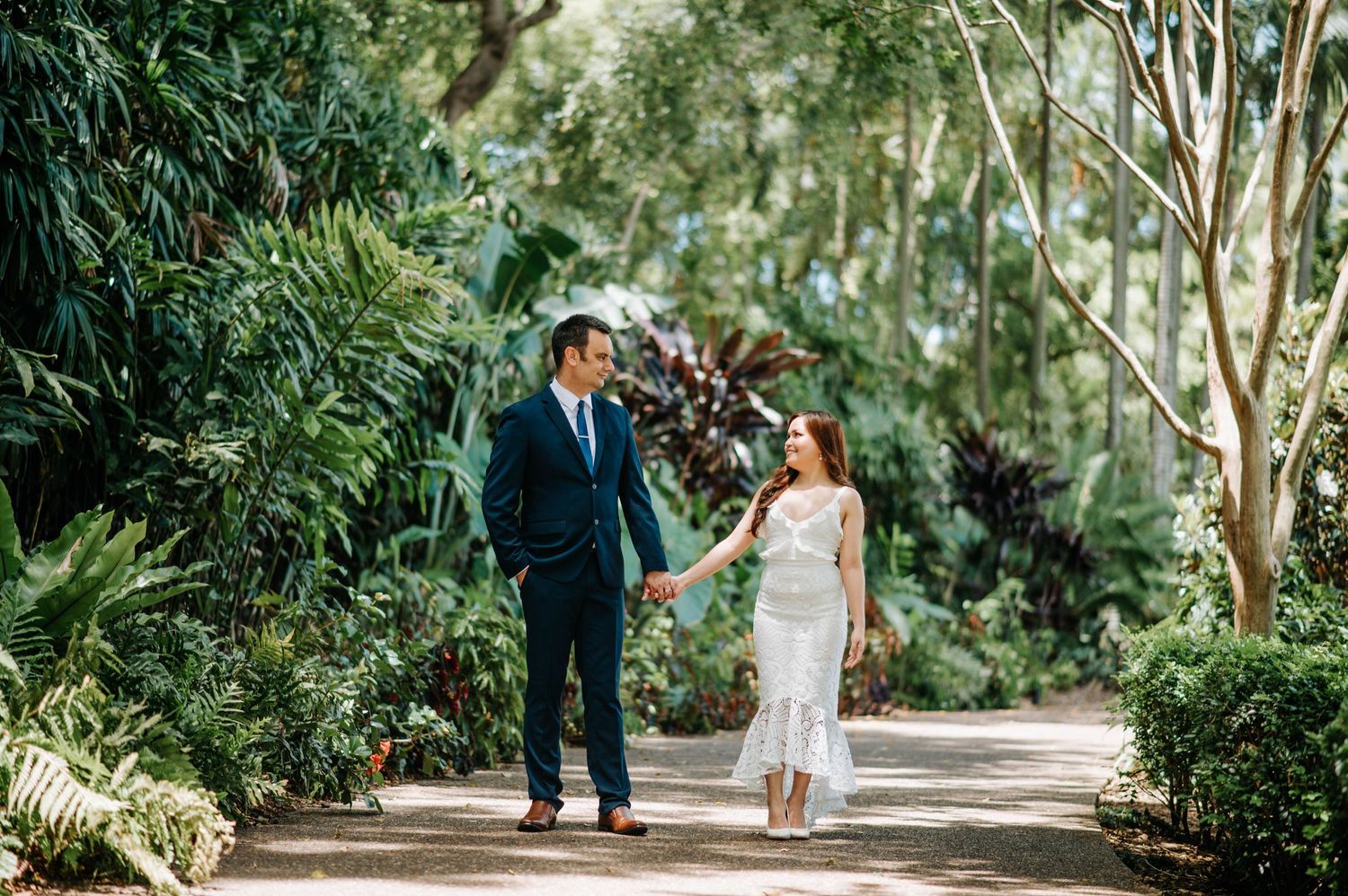 Wedding couple walking together on a lush garden path surrounded by greenery.