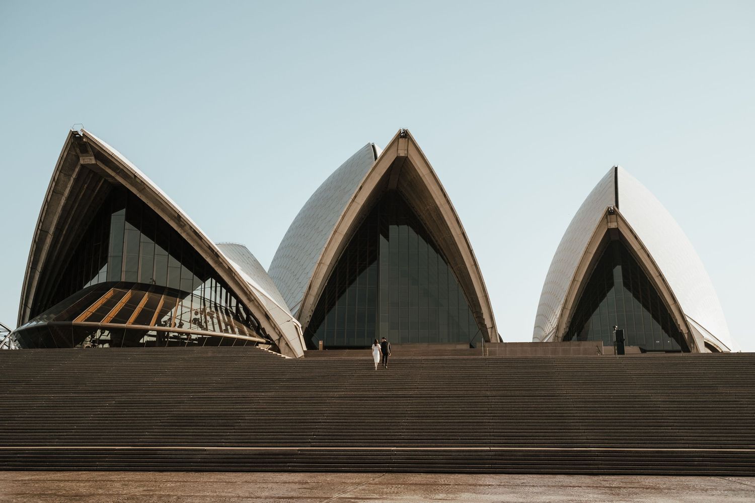 The iconic sail-shaped roof architecture of the Sydney Opera House against a blue sky.