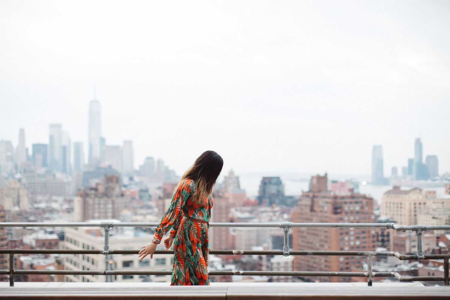 Person in colorful dress looking at NYC skyline from rooftop terrace.