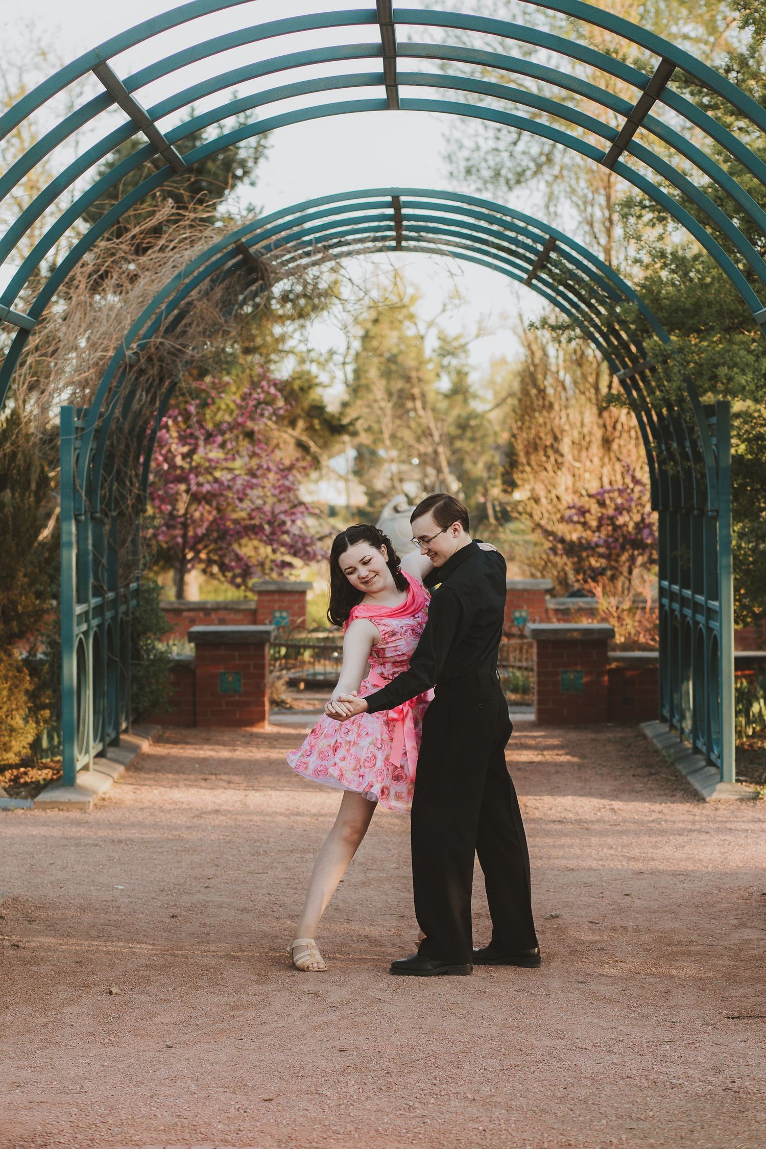 Romantic couple dancing under green garden archway during golden hour.