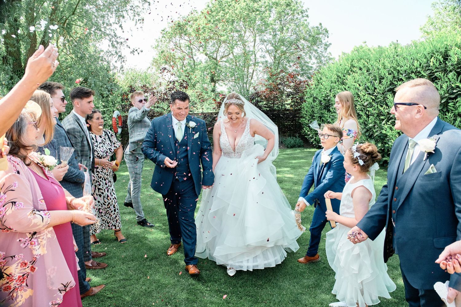 Wedding celebration in a garden with guests throwing confetti during the recessional walk.
