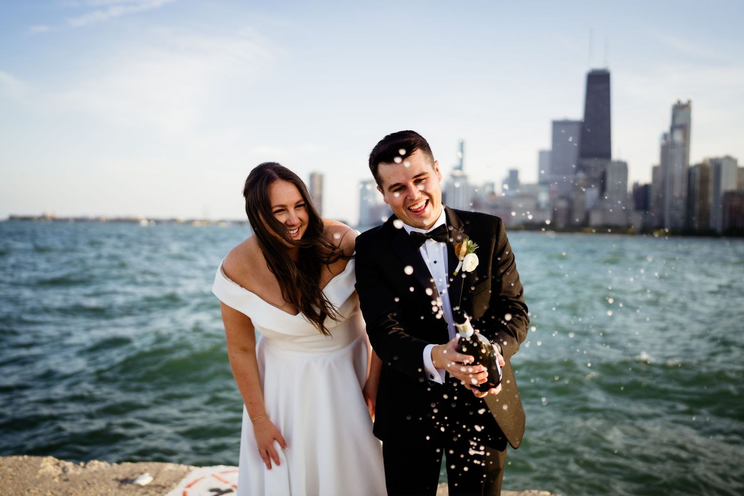 Couple popping champagne by Lake Michigan with Chicago skyline in background.