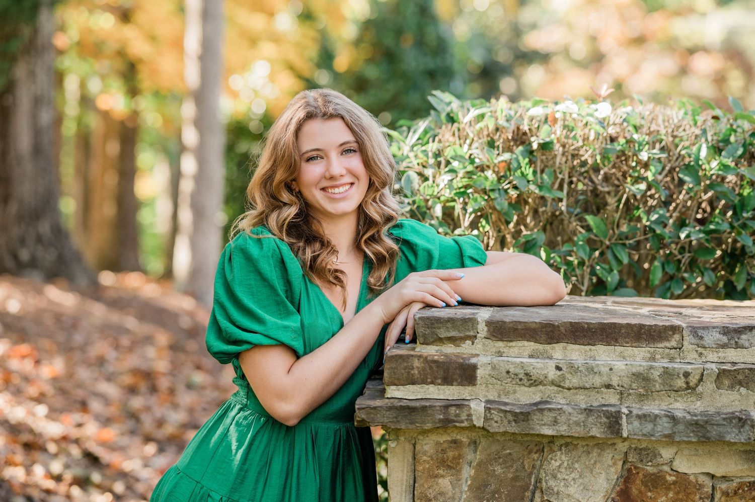 Outdoor portraits by a stone wall with green foliage in the background.