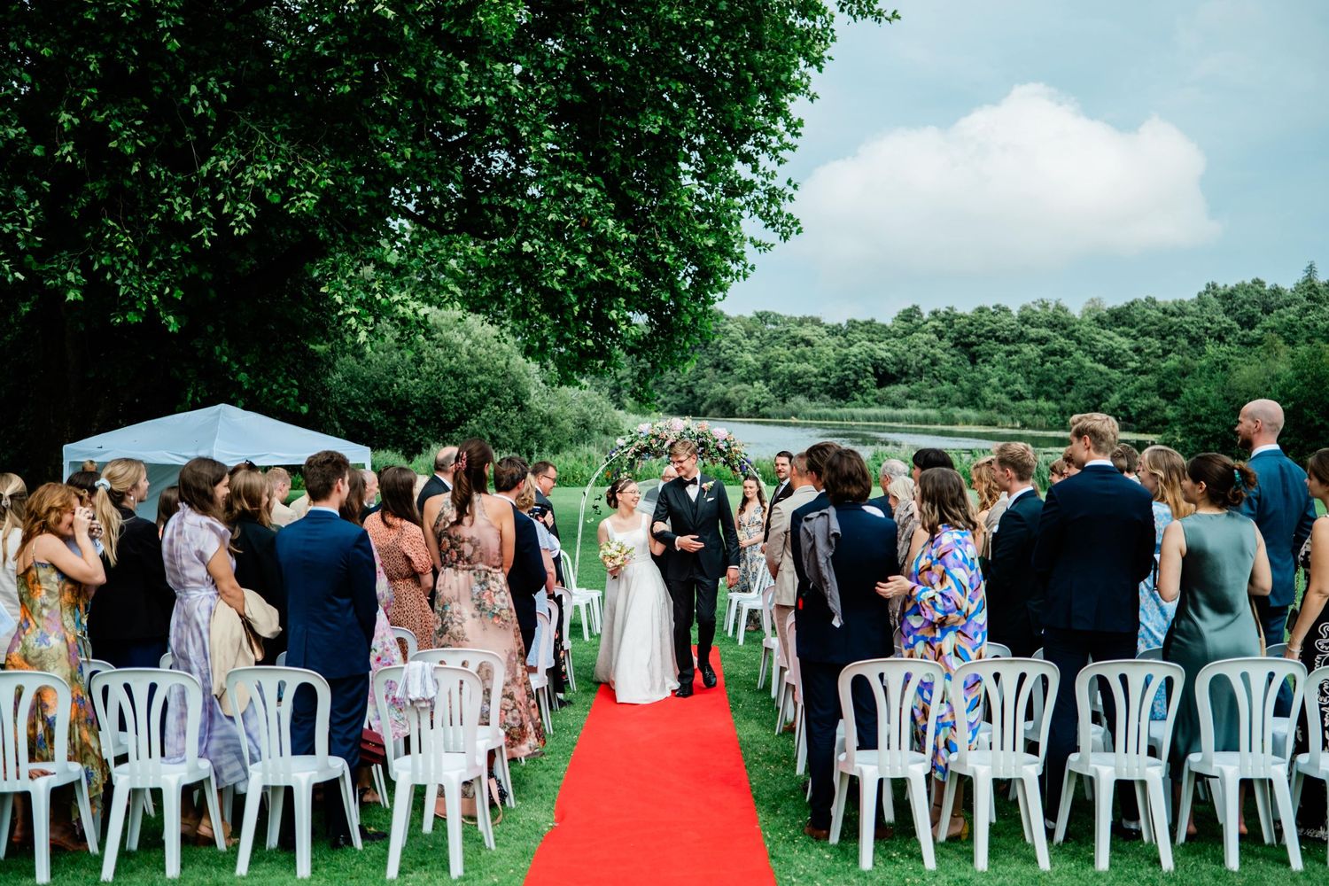 Outdoor wedding ceremony setup with white chairs and red aisle runner.