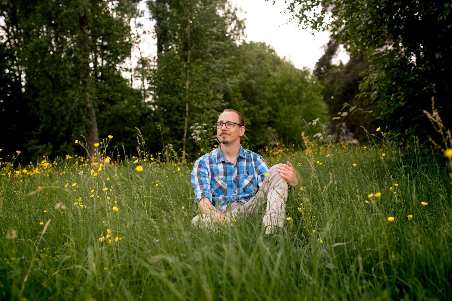 Person sitting in field of tall grass and yellow wildflowers during golden hour.