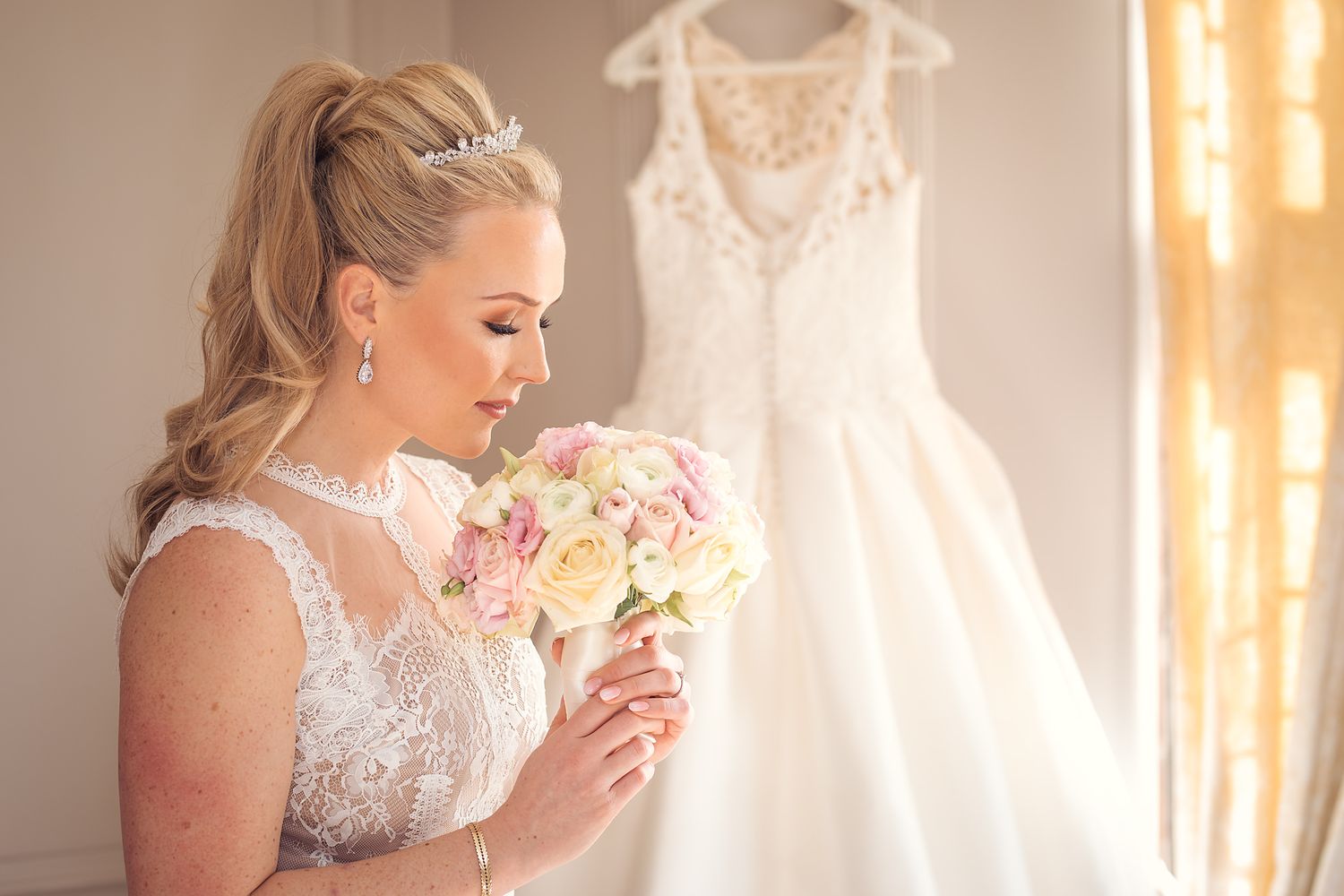Elegant bridal preparation scene with pink bouquet and white dress hanging in sunlit room.