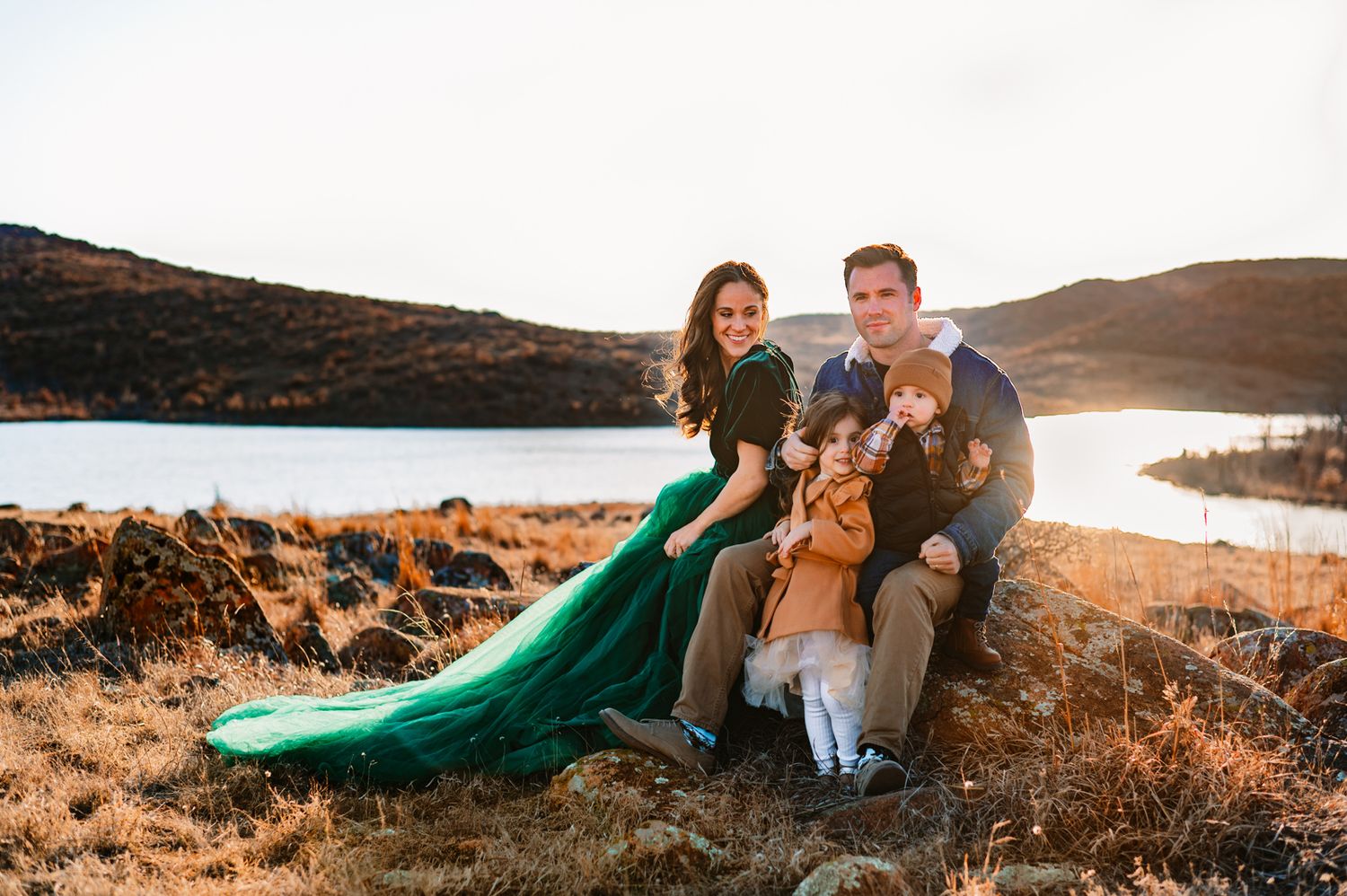 family photoshoot in oklahoma mountains; family of 4 seated on rock in front of large body of water during family photo session