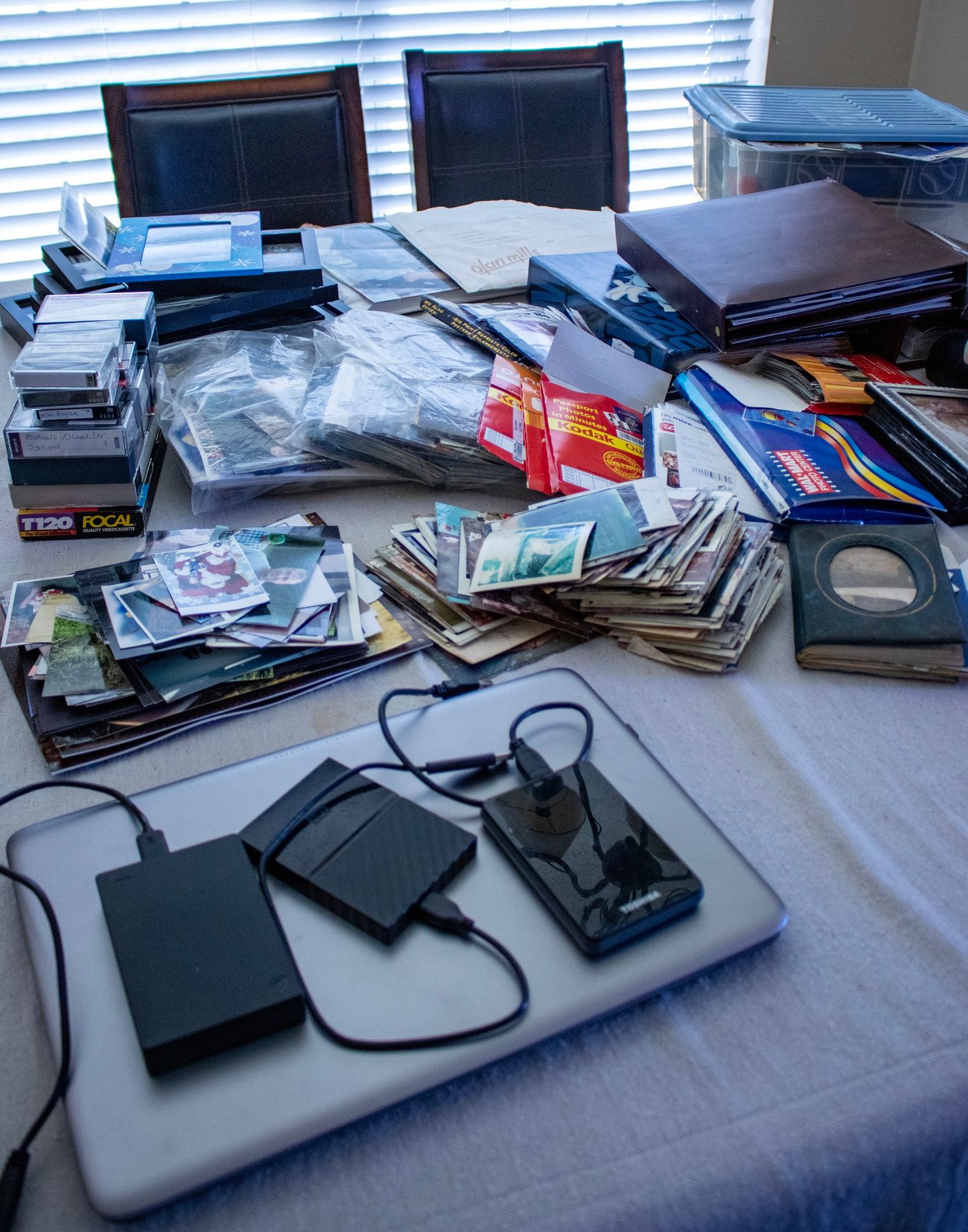 Multiple printed photos, VHS tapes, and laptop on a table