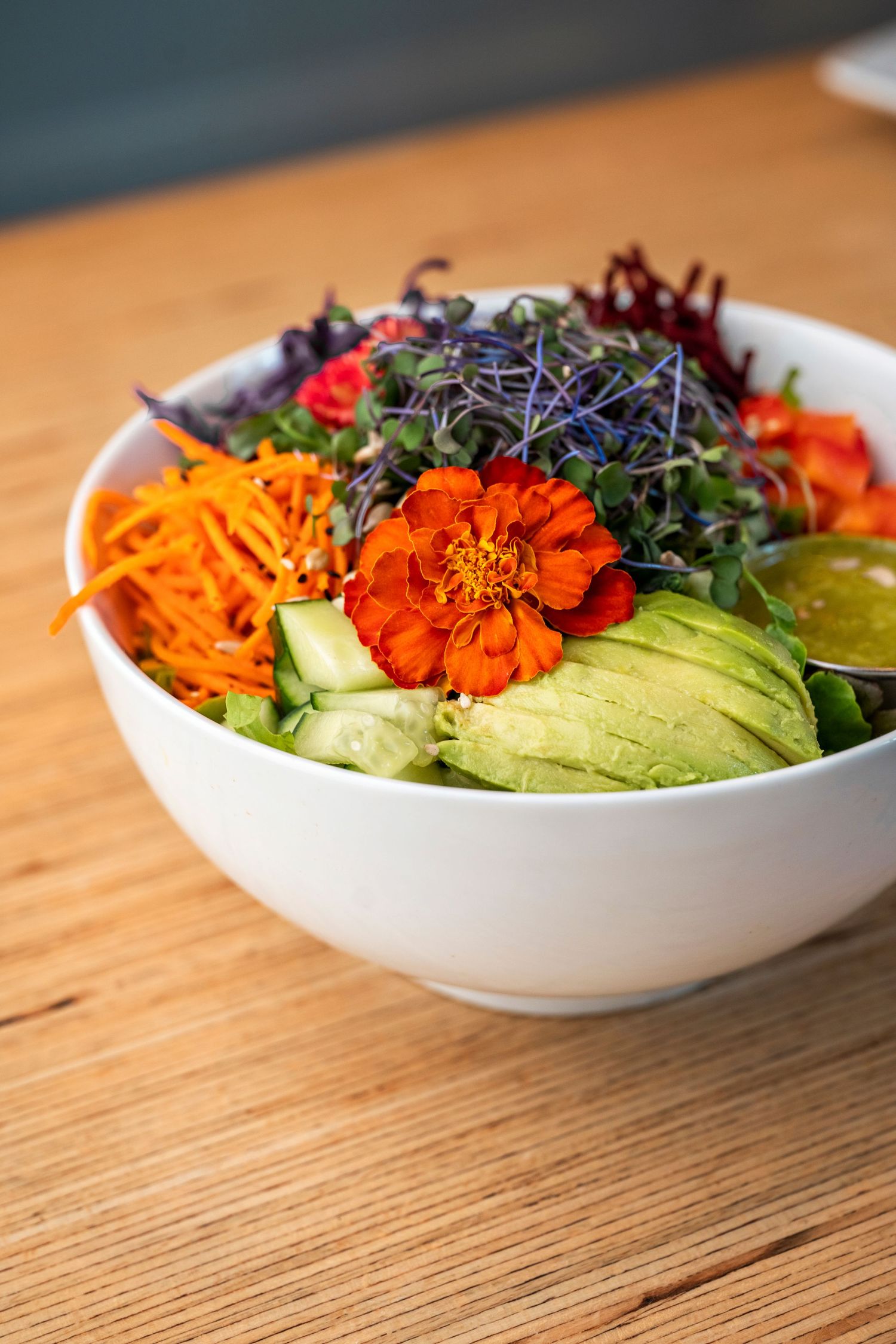 Colorful bowl of fresh salad with avocado, carrots, and edible flowers on wooden table.