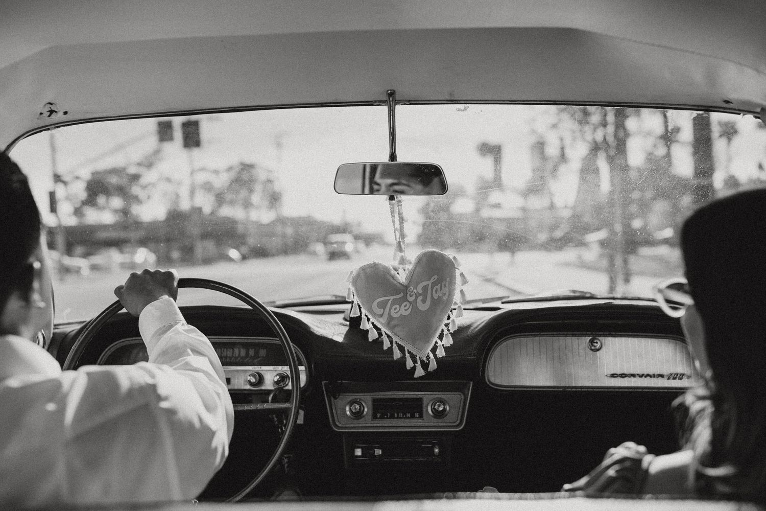 Black and white interior view of vintage car with heart ornament hanging.