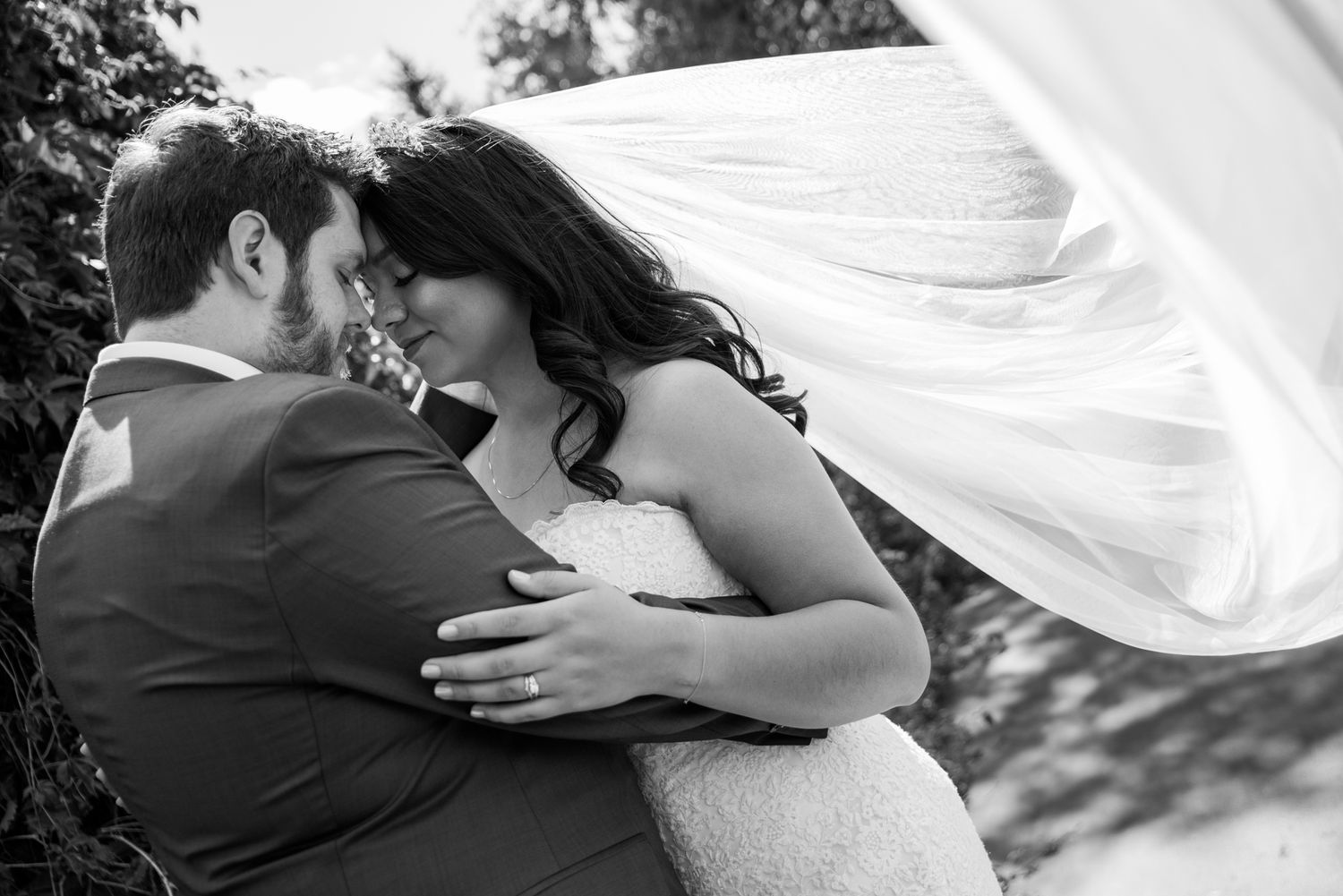 An intimate black and white wedding portrait with a flowing veil in the breeze.