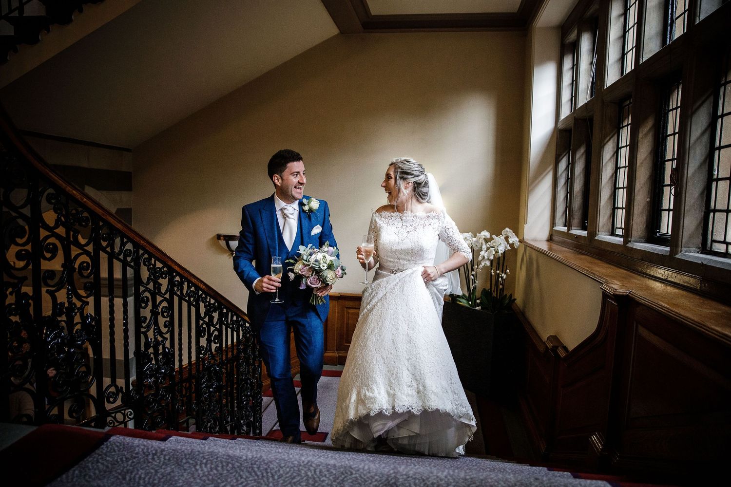 Wedding party walks down an elegant indoor staircase in formal attire.