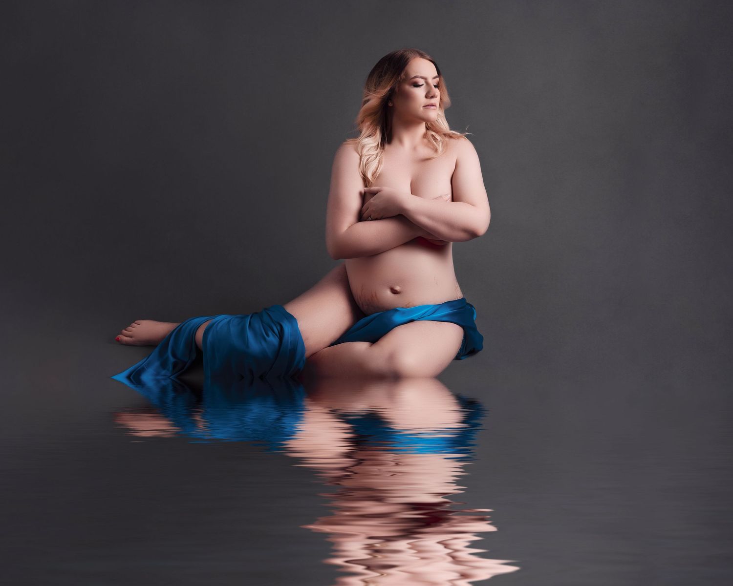 Artistic water reflection portrait with flowing blue fabric in dark studio setting.