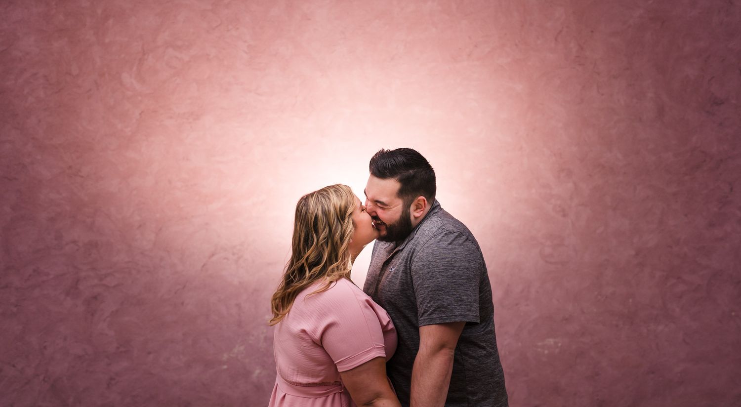 Romantic couple sharing an intimate moment against a brick wall in soft lighting.