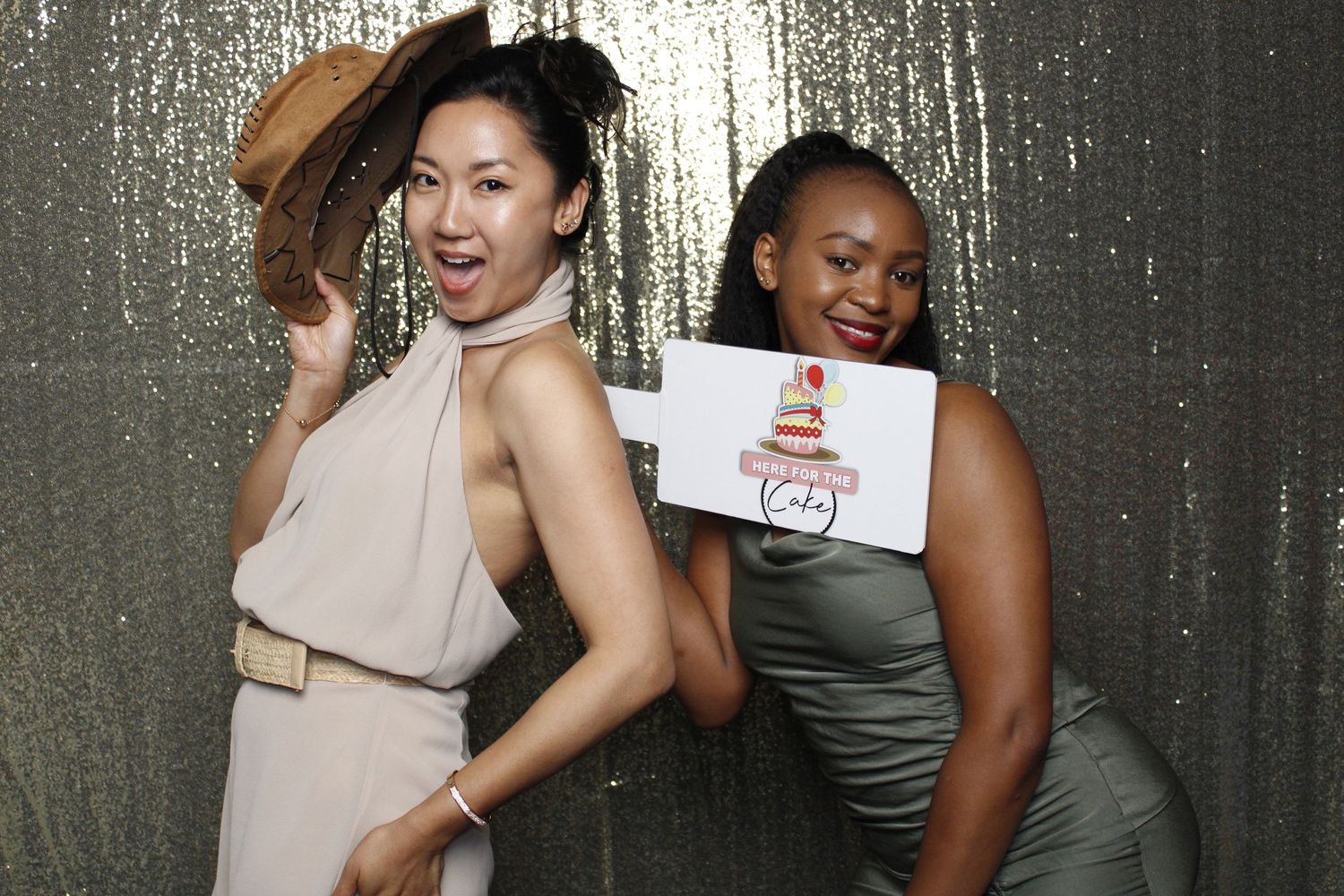 Two friends posing and having fun in a photo booth with silver backdrop.