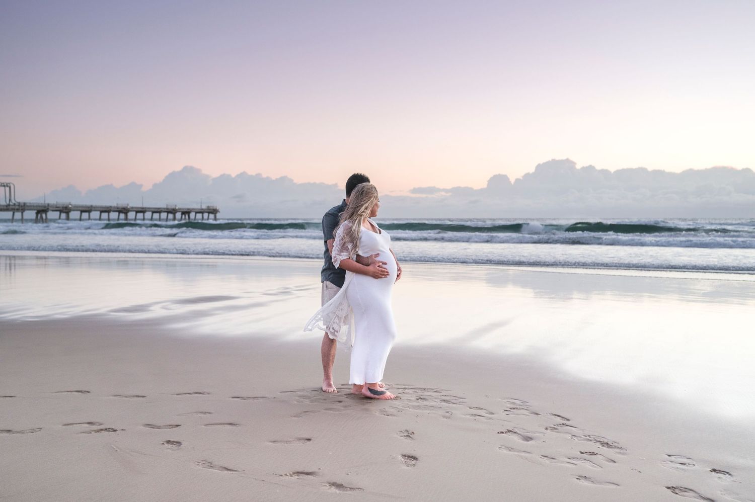 Romantic beach maternity portrait at dusk with pier in background.