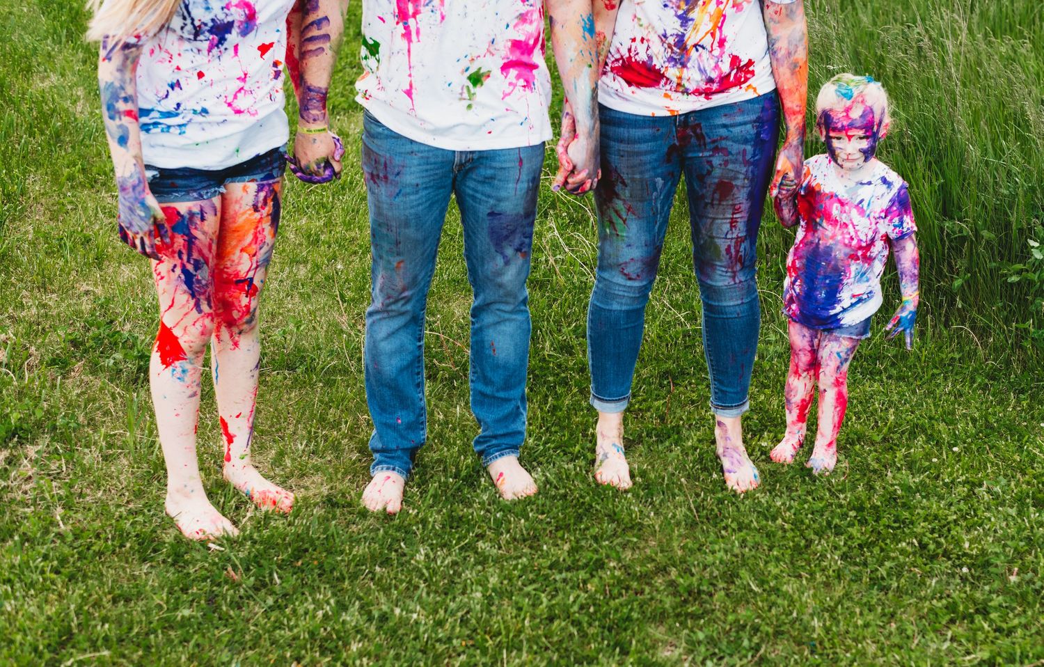 Group wearing paint-splattered clothes standing barefoot on grass.