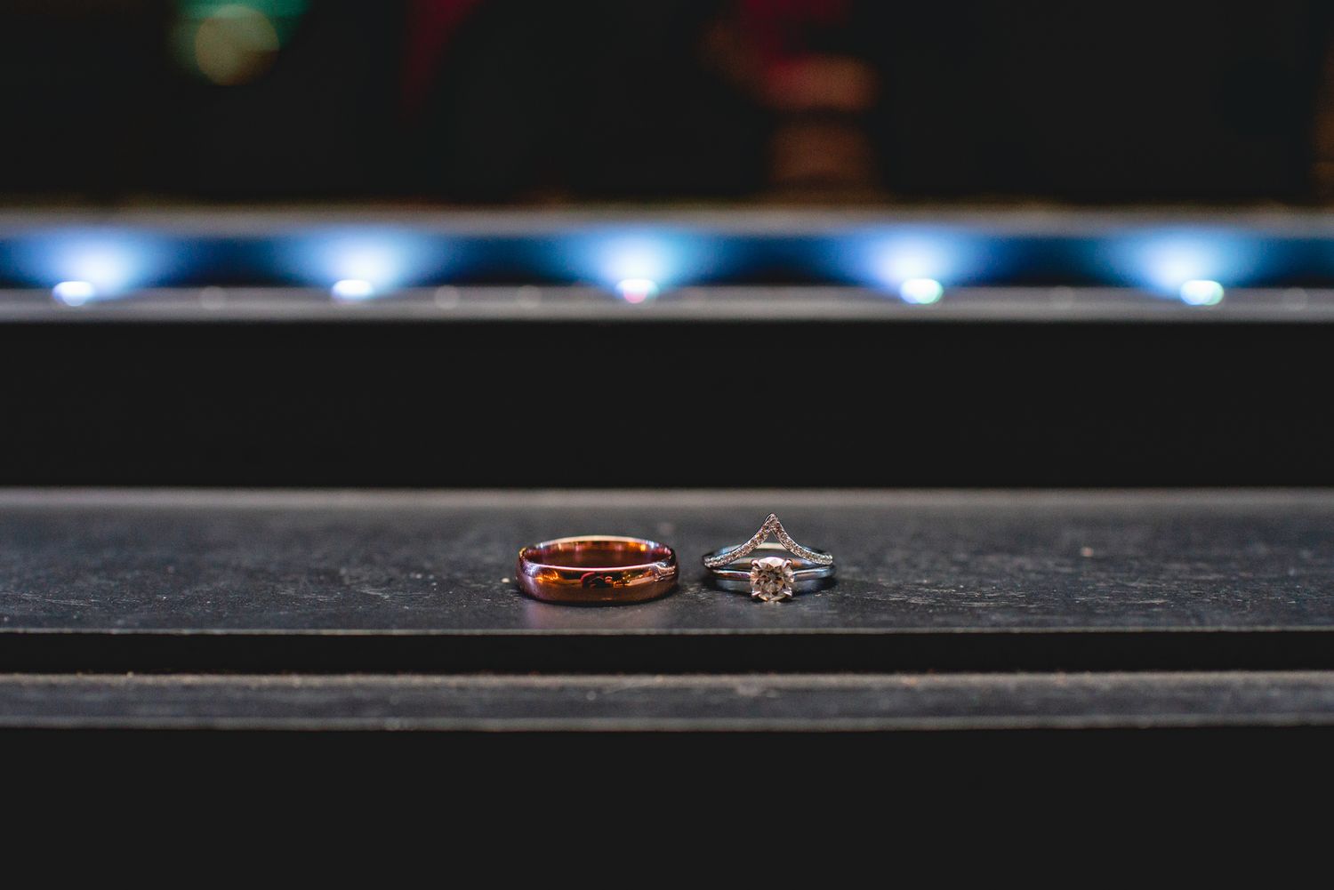 Two wedding rings photographed on a dark surface with blue lighting in the background.