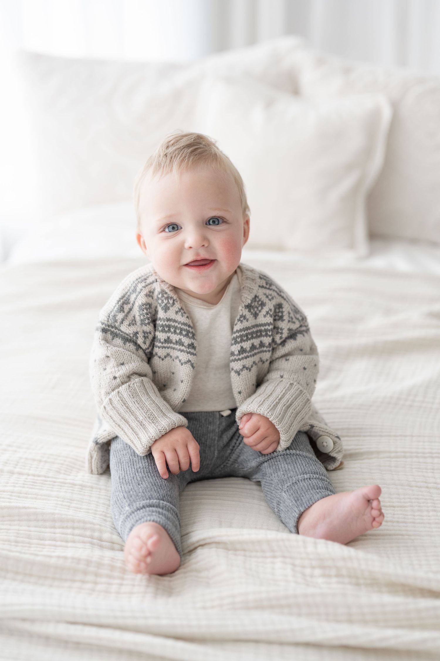 Bébé de 9 mois souriant sur un lit blanc lors d'une séance photo simplicité pour souligner les étapes de son développement