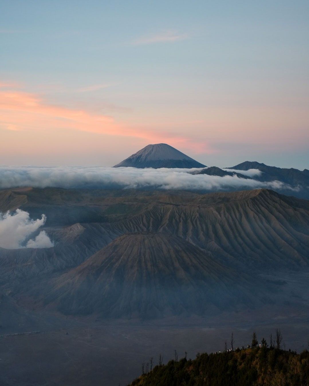 Aerial view of Mount Bromo volcano at sunrise with misty clouds and rugged terrain in East Java, Indonesia.