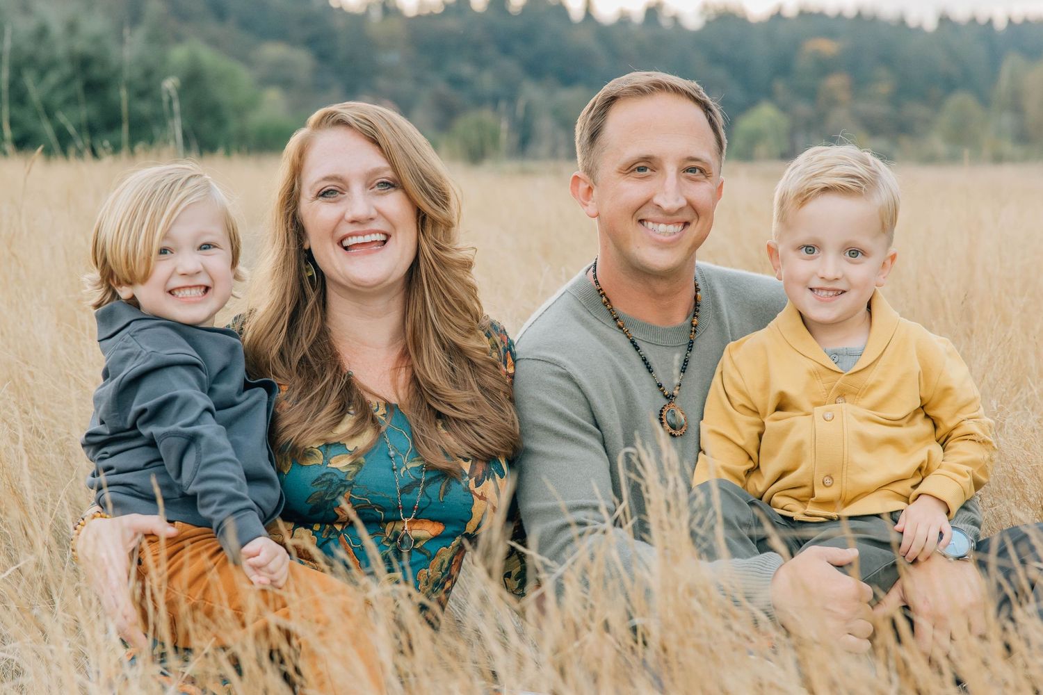 Happy family of four smiling together in golden field during autumn family portrait session.