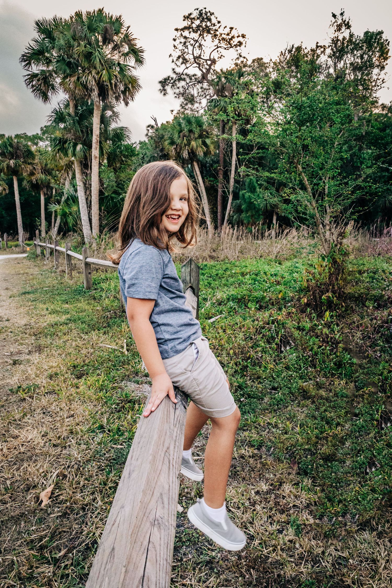 Person wearing grey t-shirt and shorts enjoys outdoor nature scene with palm trees and greenery in background.