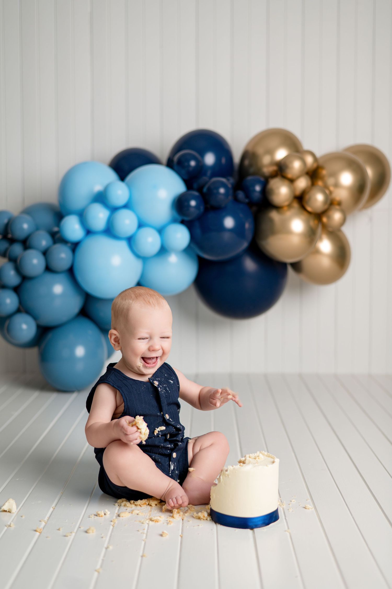 Joyful cake smash photo session with pink and white balloons on light wooden floor for first birthday celebration.