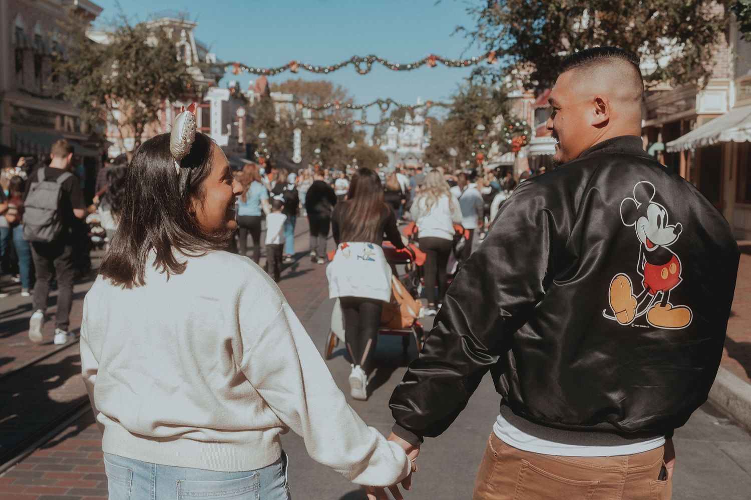 A couple walking hand in hand down a Disney theme park street adorned with decorative garlands.