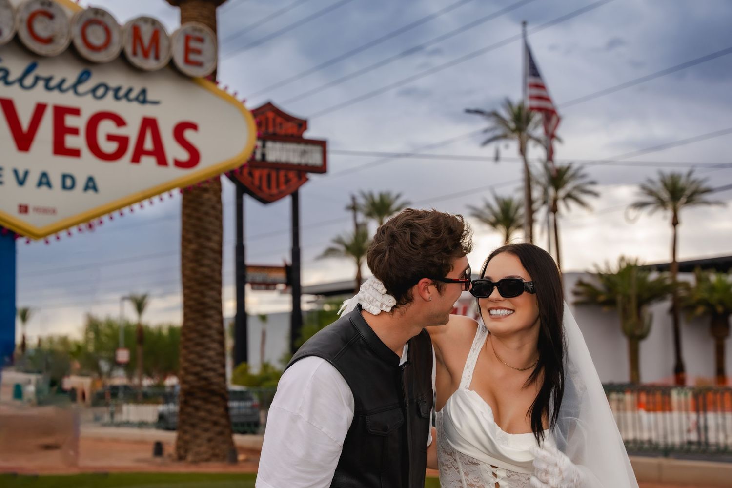 A couple celebrates their wedding day near the iconic Welcome to Las Vegas sign with palm trees in the background.